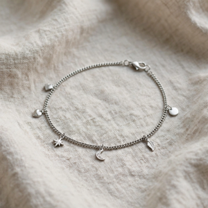 Illustrative styling image of a stainless steel ankle bracelet with small charm details