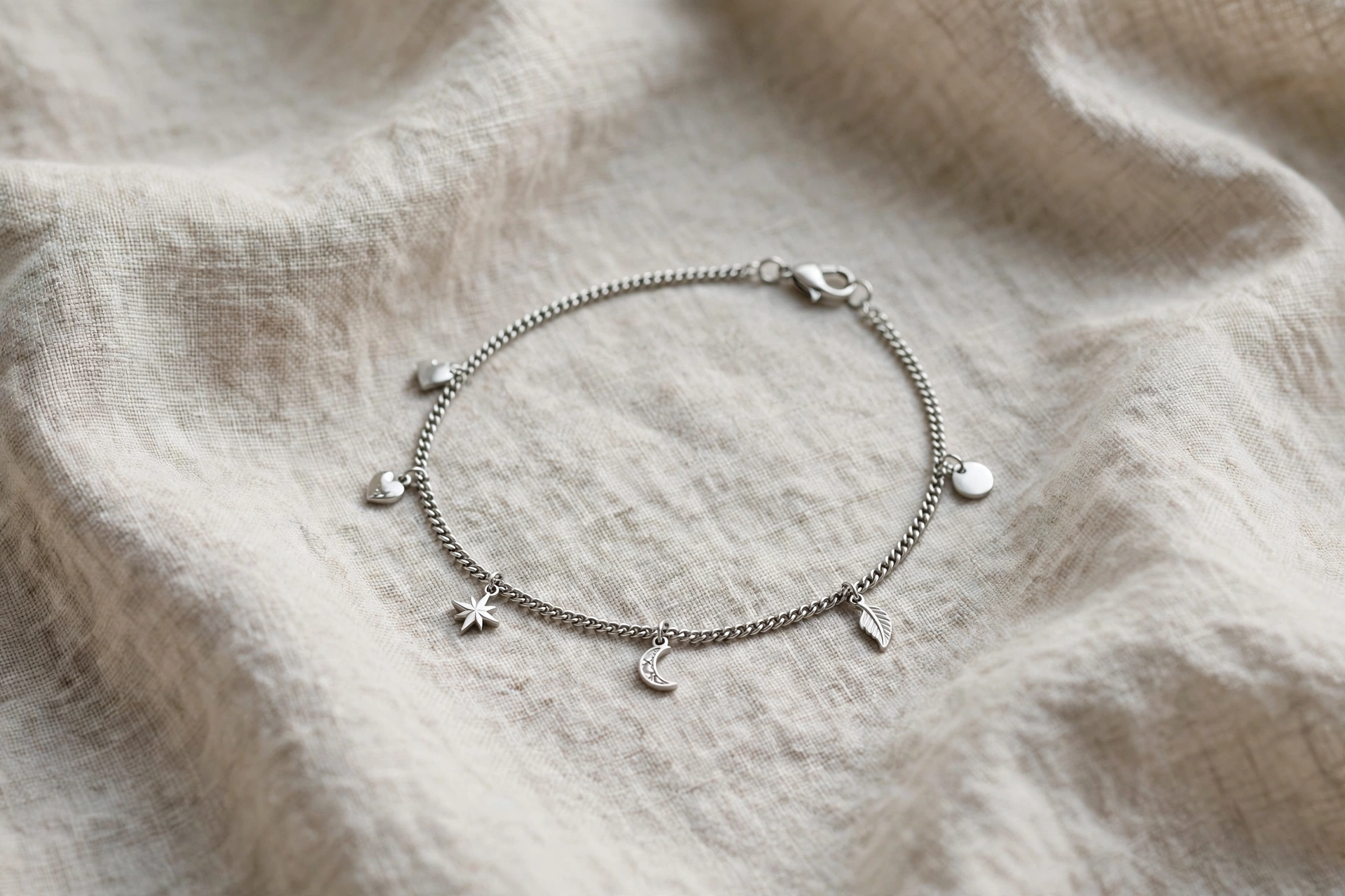 Illustrative styling image of a stainless steel ankle bracelet with small charm details