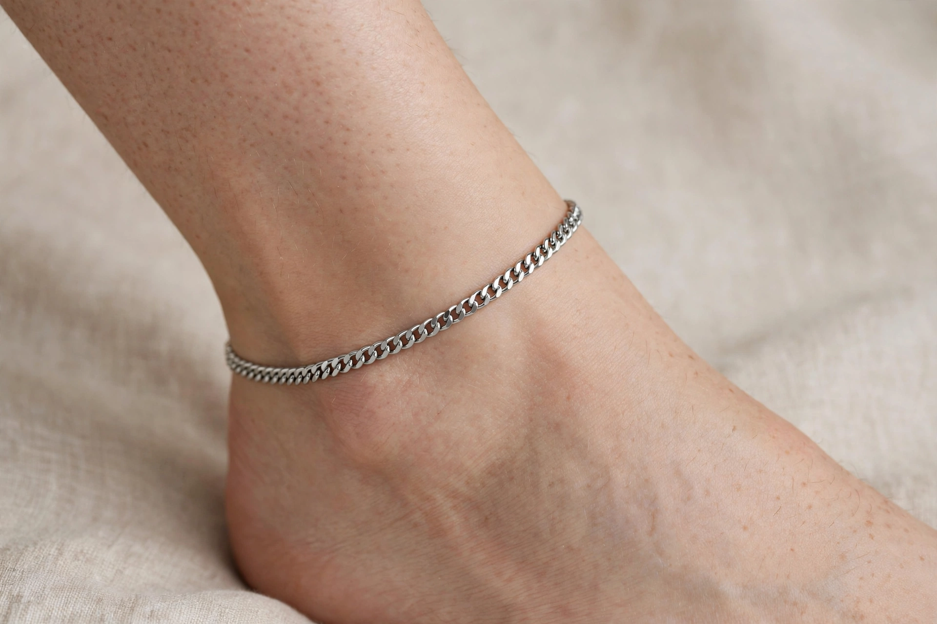 Illustrative styling image of a stainless steel ankle bracelet worn on the ankle