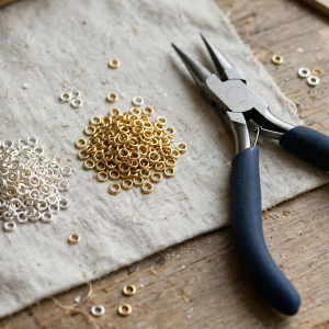 Illustrative styling image of silver and gold jump rings with jewellery pliers on a workbench
