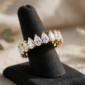 Illustrative styling image of a gold-plated eternity ring with pear-shaped stones on a display stand