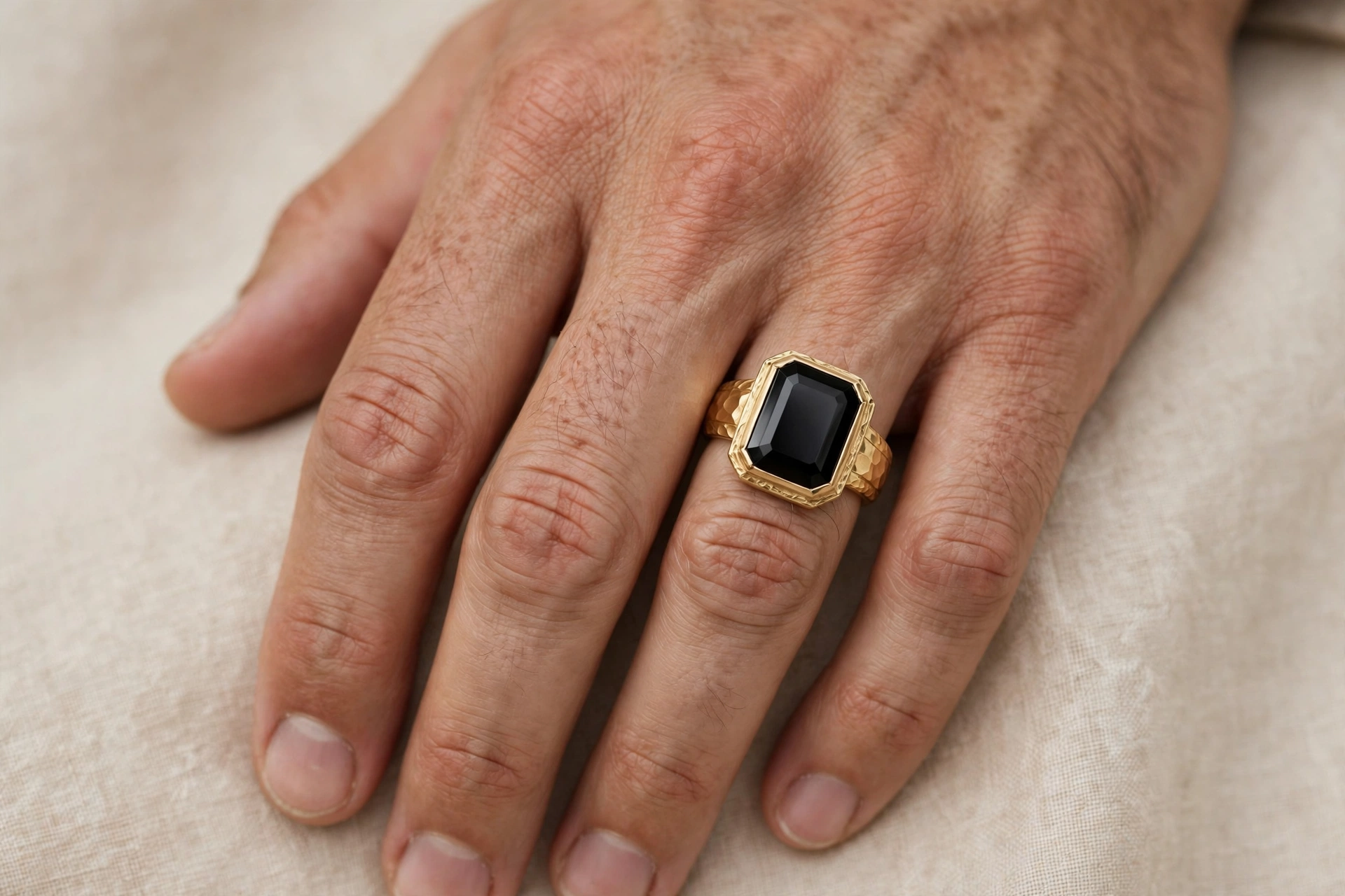 Illustrative styling image of a men's gold ring with black onyx worn on the hand
